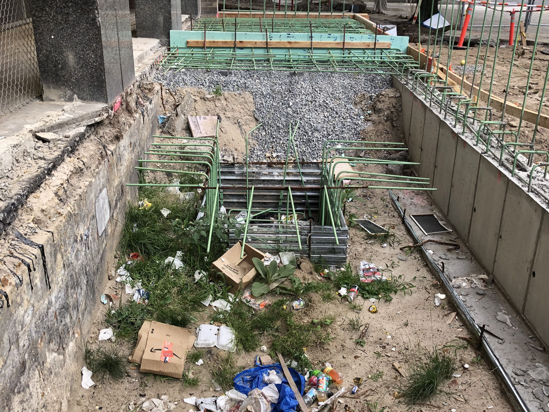 Outside the entrance of 2977 West 33rd St, a fenced portion of the ground has been opened up and been left behind by contractors, accruing mounds of garbage over time, July 6th, 2022